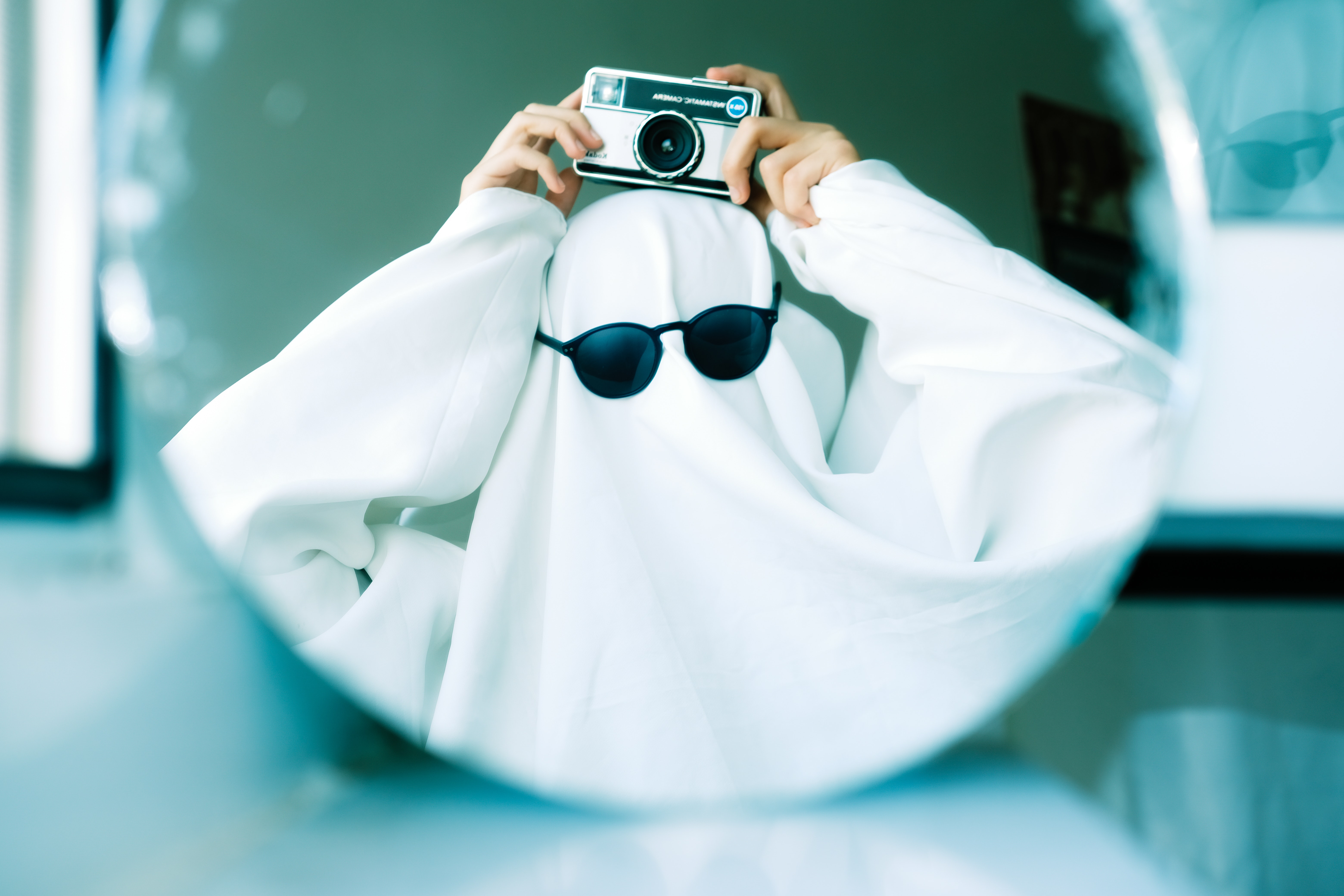 person standing in a diy halloween costume as a ghost withe a white sheet on their head and sunglasses